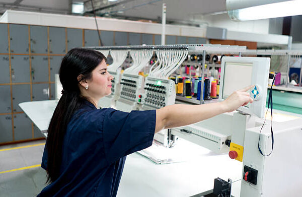 Latin American woman operating the embroidery machine at a clothing factory - fashion industry concepts