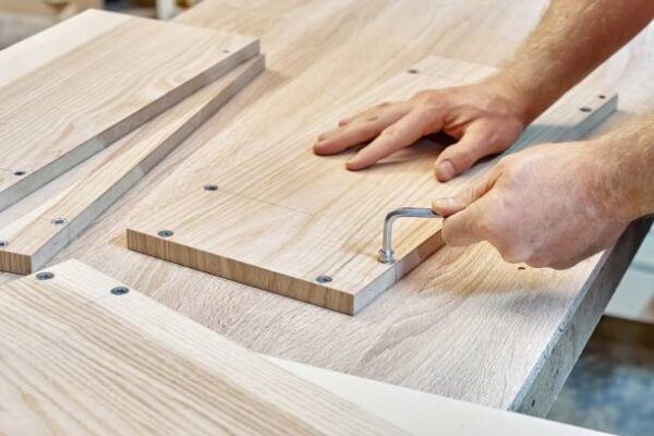 Carpenter assembles wooden furniture, twists the fittings into the veneered panel on workbench in the workshop