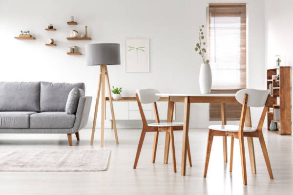 Wooden chairs at table in bright open space interior with lamp next to grey couch