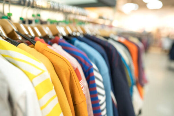 Clothes on hangers - new fashion collection at fashionable clothes store. Clothing rental or secondhand store concept. Clothes stall against blurred store background with copy space